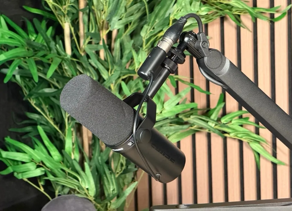 Shure SM7dB broadcast microphone on a boom arm in front of green plants and slatted wooden panelling