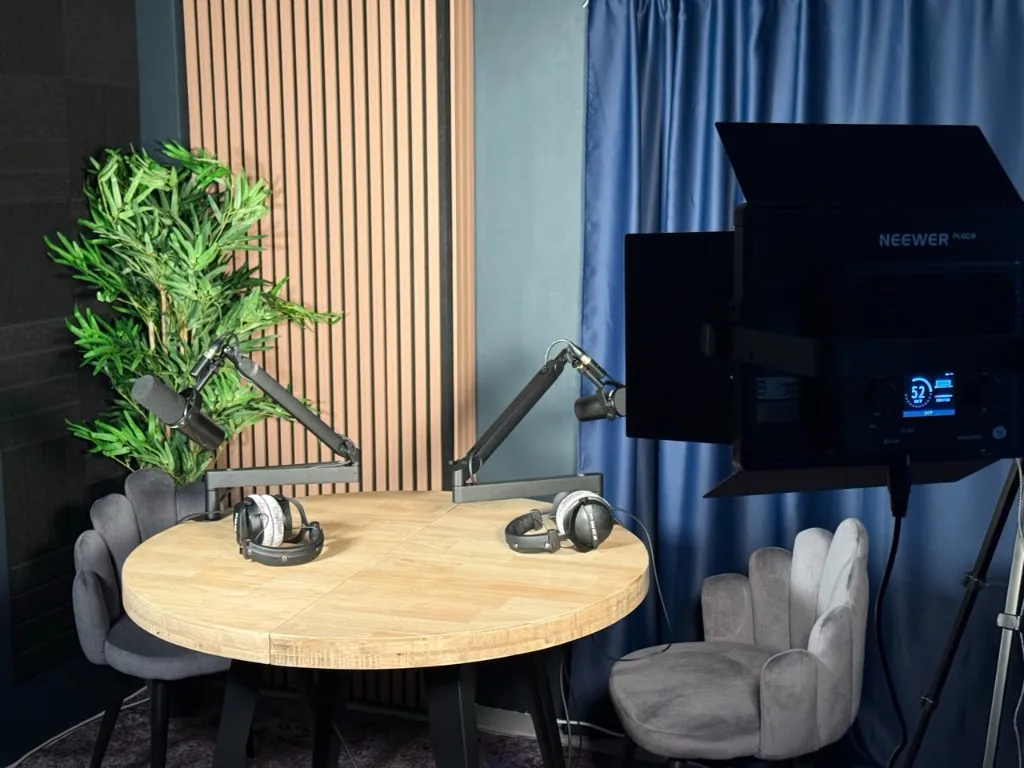 Inside the Gibraltar podcast studio: two Shure SM7dB microphones on boom arms over a round oak table, with headphones, velvet chairs and a professional LED light